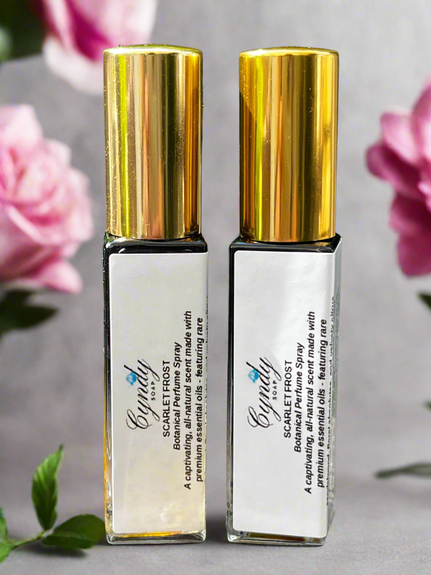 Two bottles of Elegantly Scarlet Frost Botanical Perfume Spray with gold caps on a gray background with pink flowers.