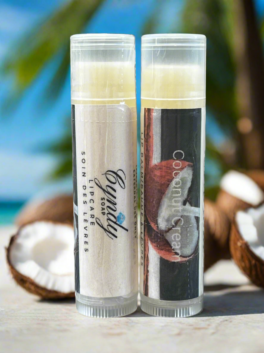 Two lip balm tubes on a beach with coconuts.