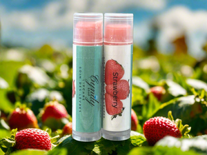 Two lip balm tubes with strawberry design in a strawberry field